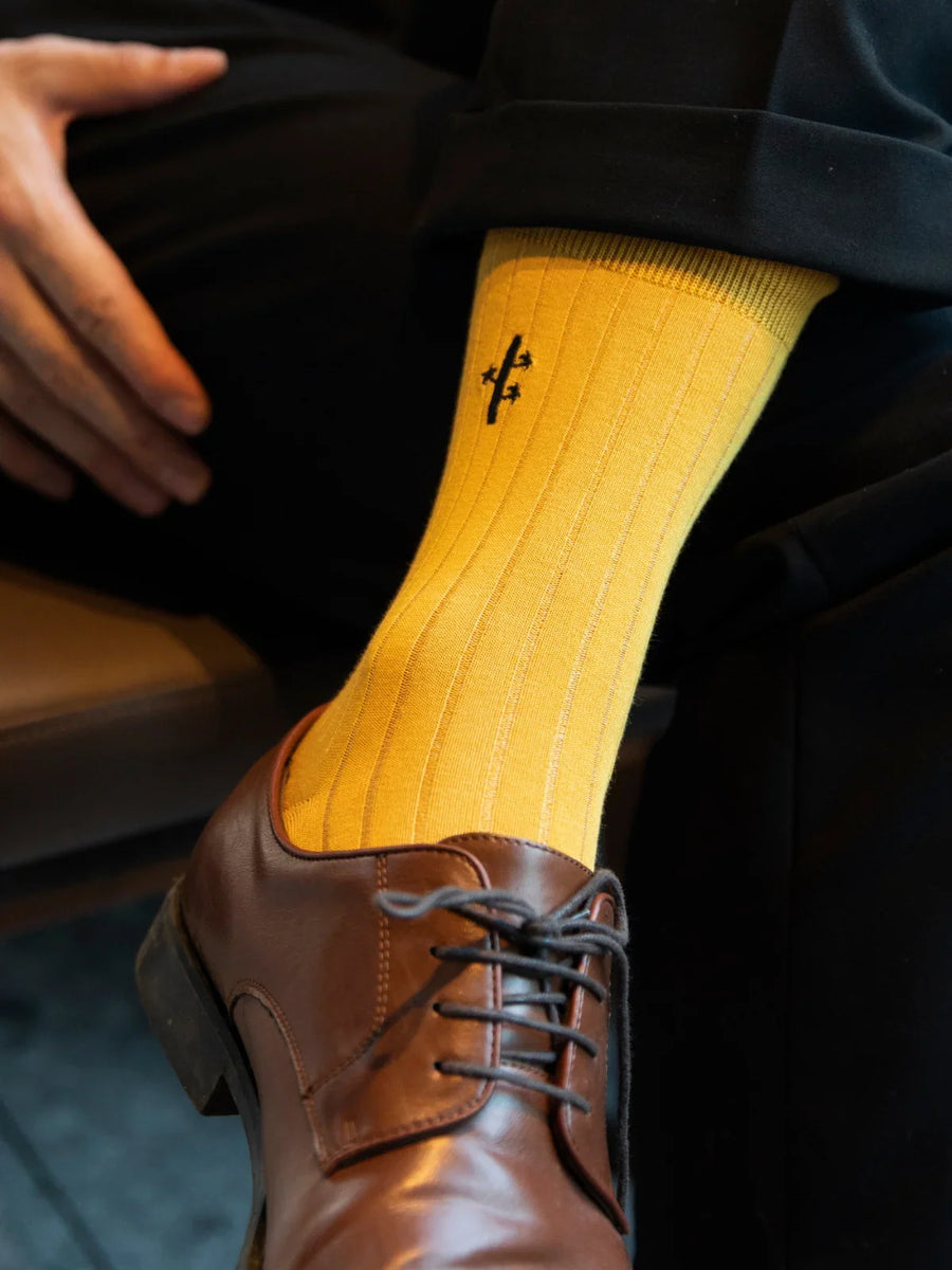 Yellow sock with a black logo worn with brown dress shoes.