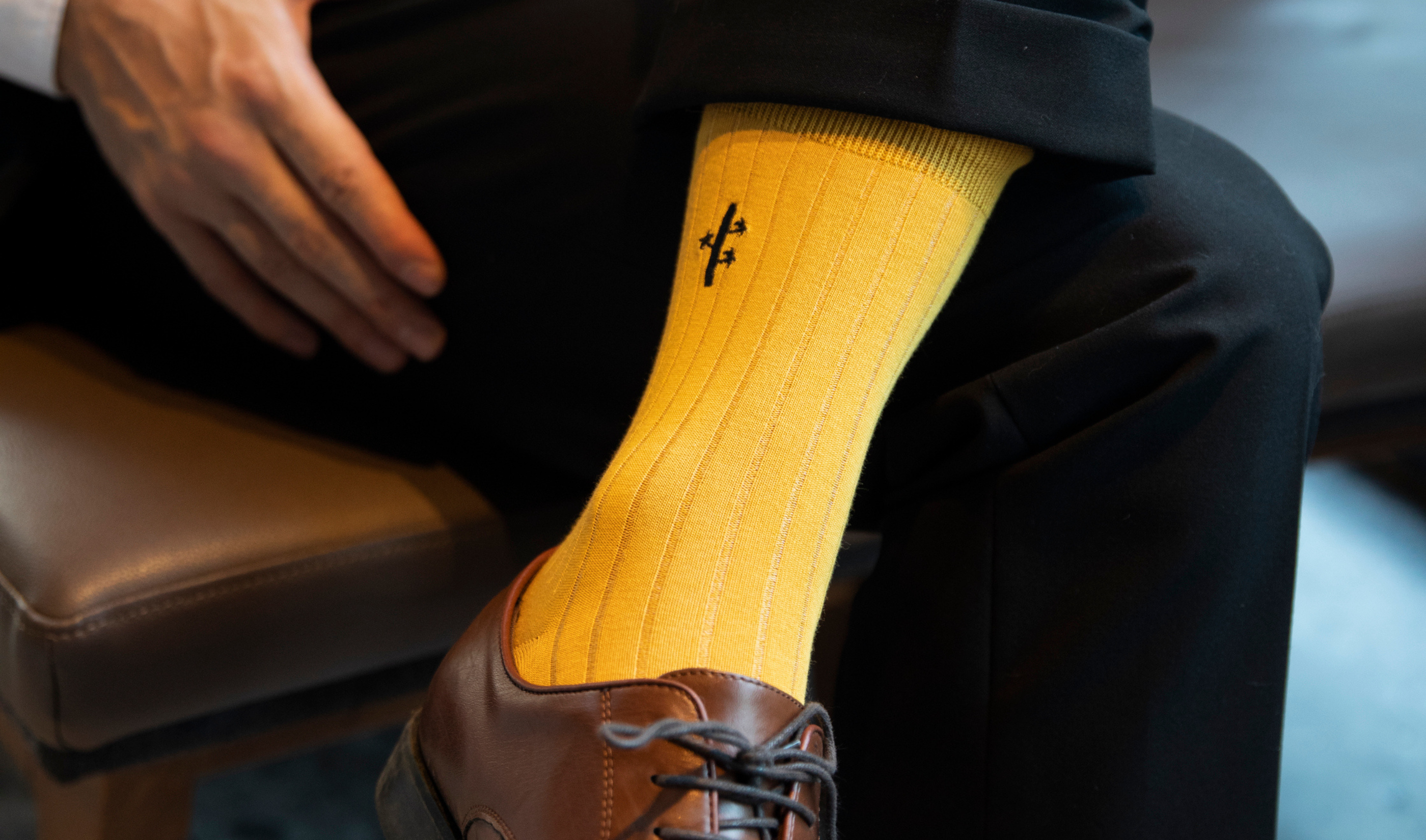 Yellow sock with a brand logo worn by a person sitting on a chair.